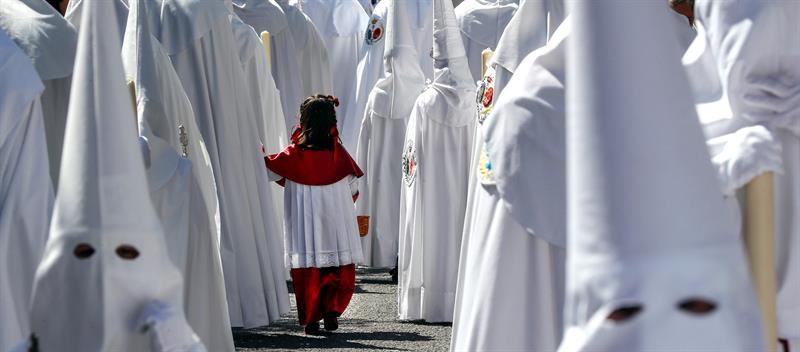 Una niña acompaña a los Nazarenos de la Paz en la estación de penitencia de su Hermandad, en la jornada en la que comienzan los desfiles procesionales del Domingo de Ramos en Sevilla. 