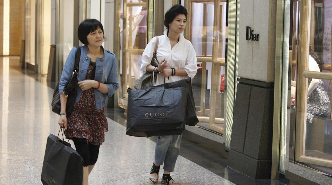 Dos mujeres caminan por un centro comercial con bolsas de compras.