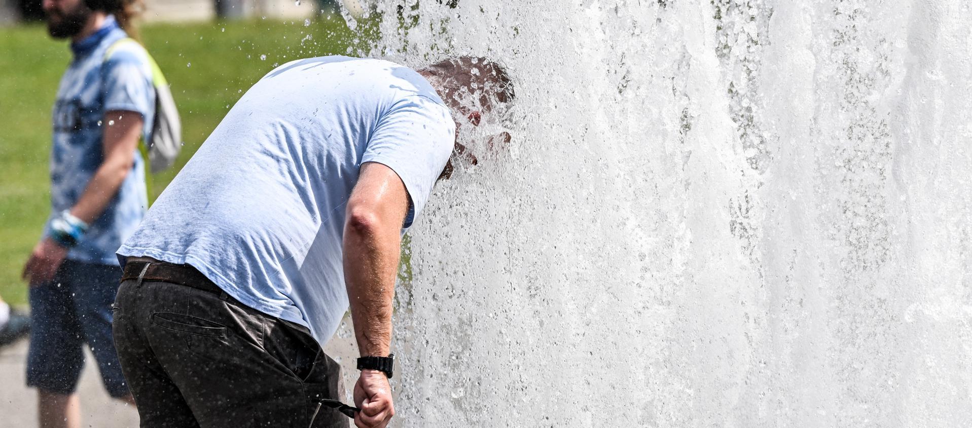 Un hombre se refresca en una fuente ante las altas temperaturas. 