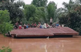 Un grupo de personas aguarda en lo alto de un tejado en una zona inundada tras el derrumbe de una presa hidroeléctrica en un pueblo cercano a la provincia de Attapeu, en Lao